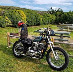 a motorcycle parked in the grass next to a wooden bench with a helmet on it