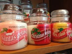 candles are lined up on a shelf in front of glass jars with santa's claws written on them