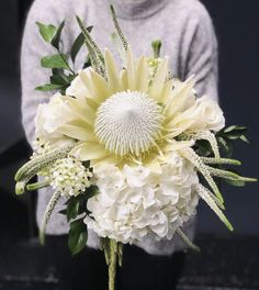 a white and yellow flower bouquet in front of a man's grey sweater with his hands behind him