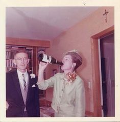 an old photo of a man and woman in formal wear drinking from wine bottles while standing next to each other