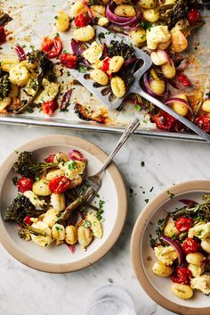 two plates with food on them next to a tray full of potatoes and broccoli