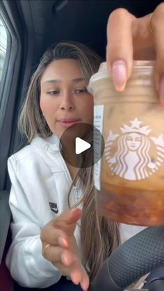 a woman is holding a starbucks drink in her hand while sitting in the back seat of a car