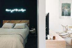 a bed sitting next to a night stand with a neon sign on the wall above it