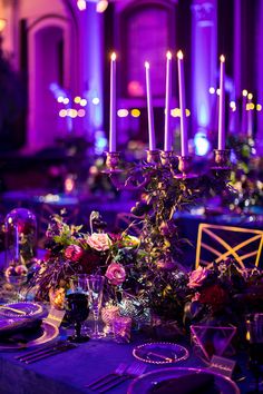 the table is set with purple candles and flowers on it, along with place settings