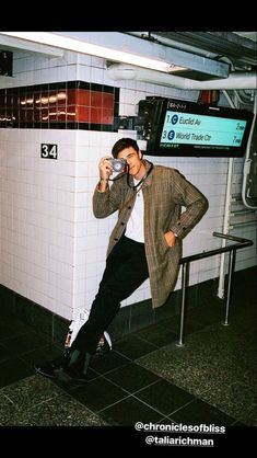 a man leaning against a wall drinking from a cup