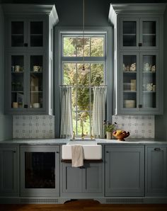 a kitchen with gray cabinets and white counter tops, an open window above the sink