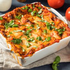 a casserole dish with tomatoes, cheese and herbs on the table next to it