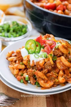 a white plate topped with pasta covered in sauce and vegetables next to other dishes on a wooden table