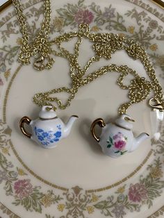 two miniature teapots on a plate with a gold chain attached to the necklace