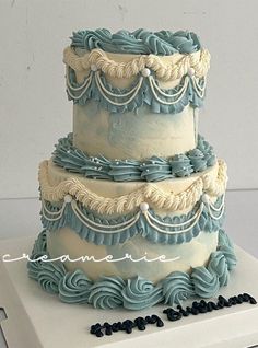 a three tiered cake with blue icing and white frosting, on top of a box