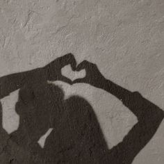 a shadow of a person making a heart with their hands on the wall in black and white