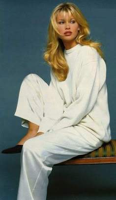 a woman sitting on top of a wooden bench wearing white clothing and high heeled shoes