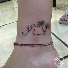 a woman's foot with a small tattoo on the ankle and palm trees in the background