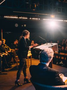 a woman standing at a podium in front of a group of people sitting on chairs