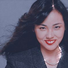 a woman with long black hair wearing a suit and smiling at the camera while holding a diamond necklace on her neck