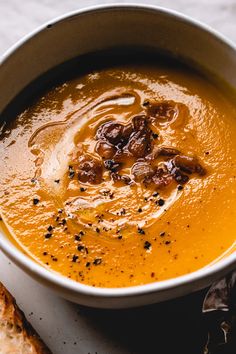 a white bowl filled with carrot soup next to some slices of bread on a table