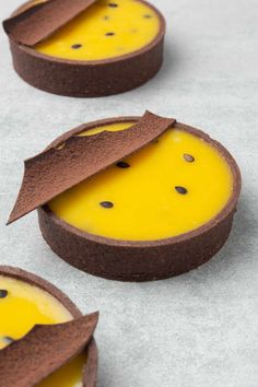 three desserts with chocolate and yellow icing in them on a gray tablecloth