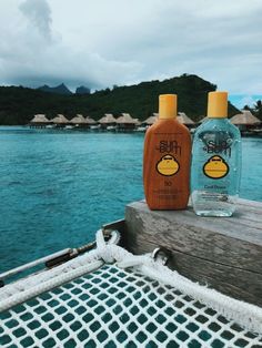 two bottles of mouthwash sitting on top of a wooden dock next to the ocean