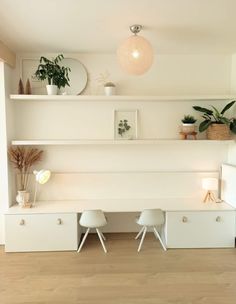 two white chairs sitting on top of a wooden floor next to a shelf filled with potted plants