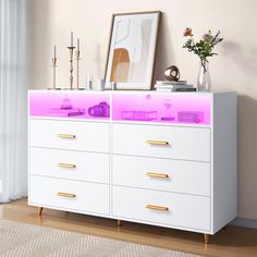 a white dresser with pink lights on the top and drawers below it, next to a window