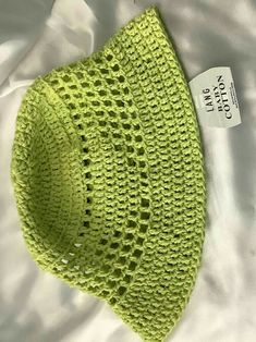 a crocheted green hat is laying on a white sheet with a tag attached to it