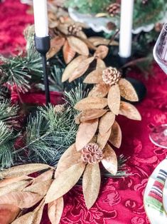 a christmas table setting with candles and greenery on the placemat, surrounded by pine cones