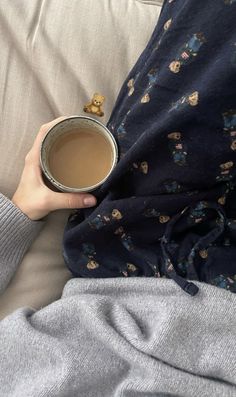 someone is holding a cup of coffee while laying in bed