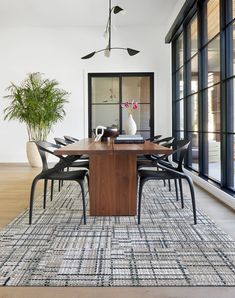 a dining room table with chairs and a vase on top of it in front of large windows