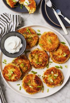 several crab cakes on a plate with sour cream and green onions next to it, along with two forks