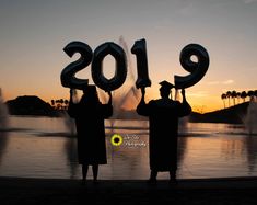 two people standing in front of a lake holding up numbers