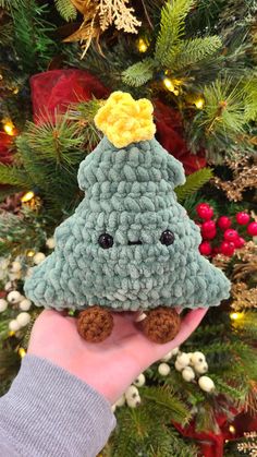 a hand holding a small crocheted christmas tree ornament in front of a christmas tree