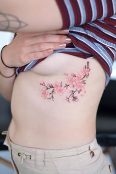 a woman's stomach with pink flowers tattooed on her belly and behind her is a striped shirt