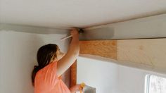 a woman in an orange shirt is working on a wall with a hammer and plywood