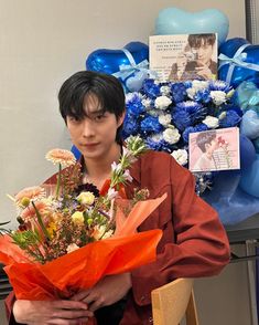 a man holding a bunch of flowers in front of a balloon wall with blue and white balloons