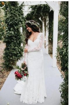 a woman in a wedding dress is standing under an arbor with flowers and greenery