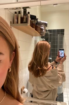 a woman taking a selfie in front of a bathroom mirror with her cell phone