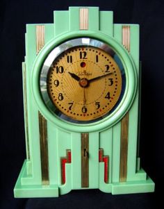 a green and gold clock with numbers on it's face, sitting against a black background