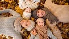 four people are laying in the leaves and posing for a photo with their arms around each other