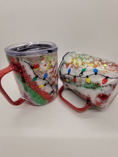 two coffee mugs with christmas lights on them sitting next to each other in front of a white background