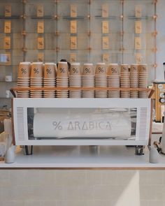 there is a coffee machine with many cups on the shelf in front of it that says arabica