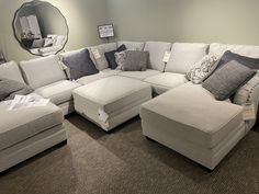 a large sectional couch with lots of pillows on the bottom and sides, in front of a round mirror