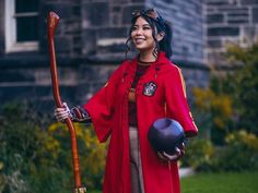 a woman in red is holding a bowling ball and a stick while standing on the grass