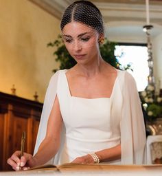 a woman in a white dress writing on a piece of paper