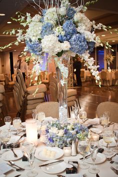 a tall vase filled with blue and white flowers on top of a dining room table