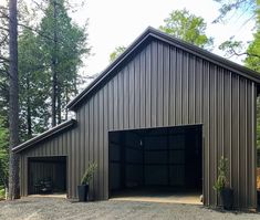 an open garage in the middle of a wooded area with tall trees and gravel ground