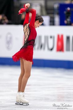 a female figure skating on an ice rink wearing a red dress and holding her arms in the air