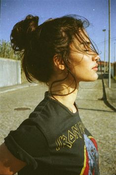 a woman with her hair in a bun is looking off into the distance while standing on a street