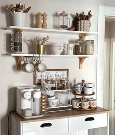 a kitchen with white walls and shelves filled with dishes, mugs and utensils