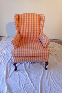 an orange and white checkered chair sitting on top of a bed covered in sheets