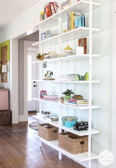 a white book shelf with baskets and books on it in a living room next to a door